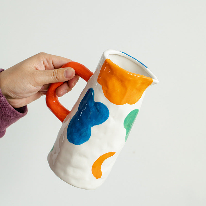 Colorful ceramic pitcher held by a hand on a white background