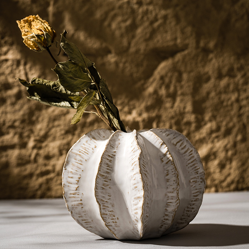 White textured vase with a dried flower against a textured brown background