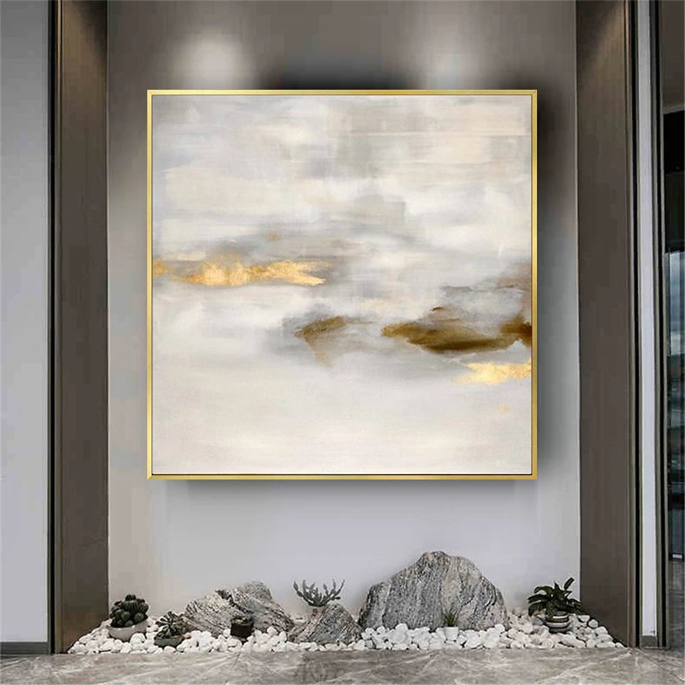 Abstract art piece with gold frame on a wall above decorative rocks and plants.