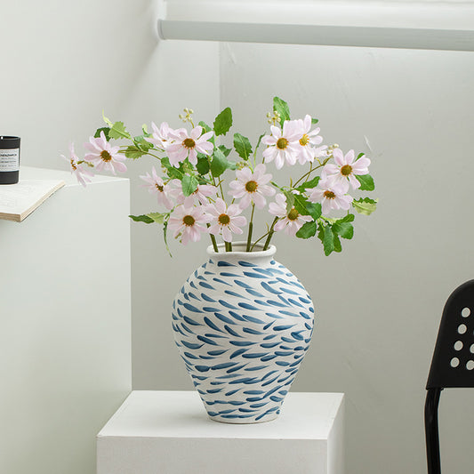 Vase with floral arrangement on a white surface against a light gray wall.