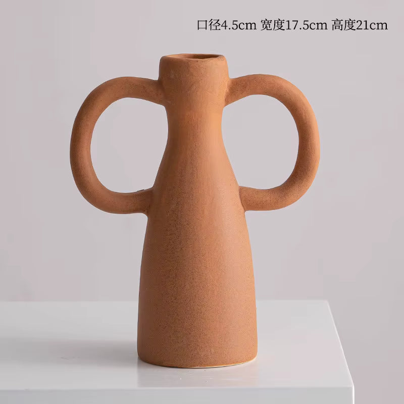 Brown ceramic vase with two handles on a white platform against a light gray background