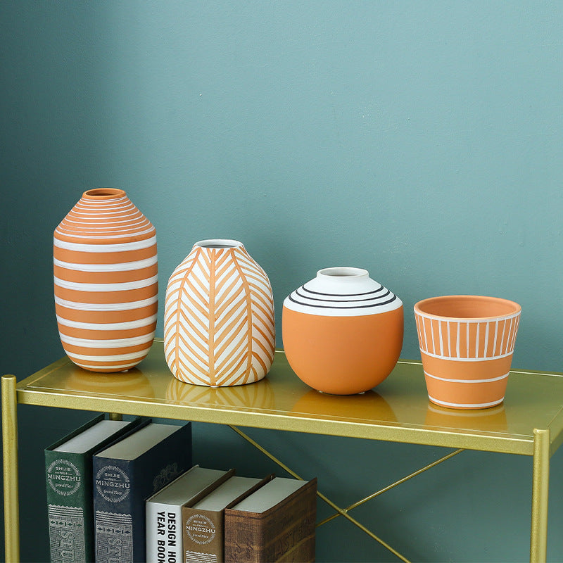 Four ceramic vases with striped patterns on a gold shelf against a teal wall.