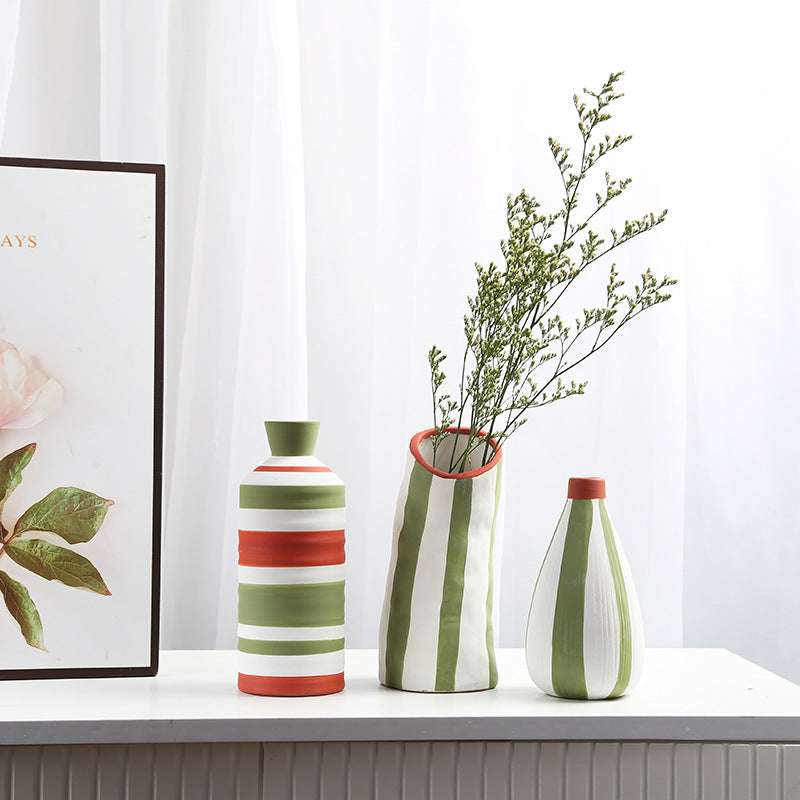 Three striped vases on a surface with a framed picture in the background
