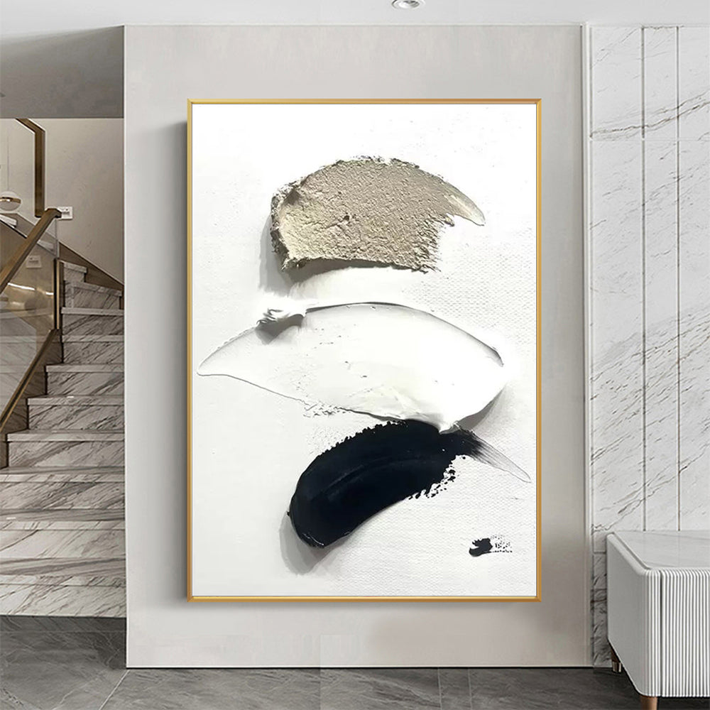 Abstract art piece with black, white, and beige colors in a gold frame on a wall.