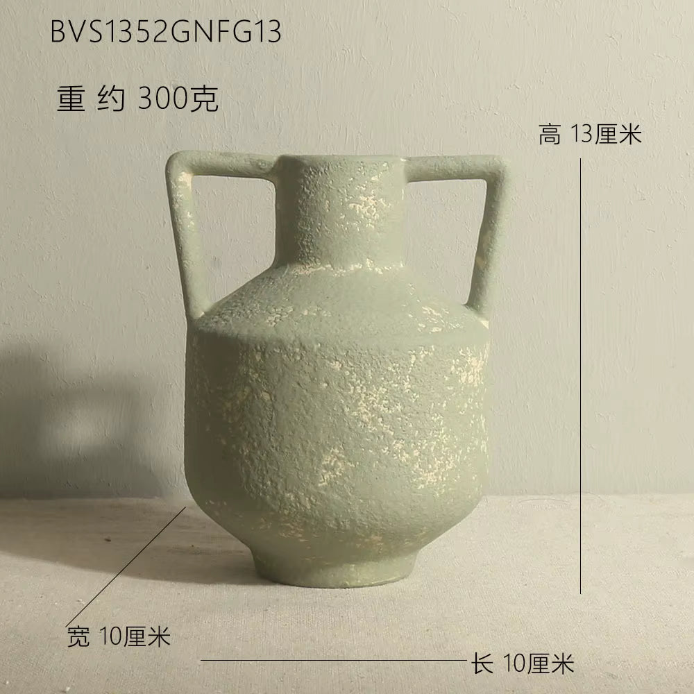 Green ceramic vase with handles on a light gray background