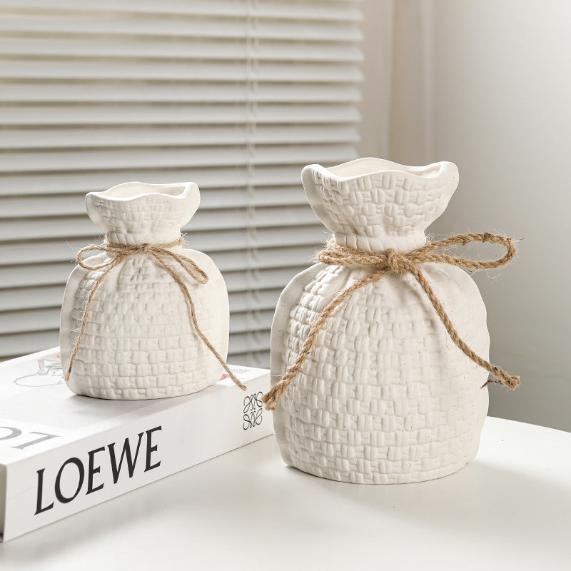 Two white textured ceramic pots with twine on a surface with a LOEWE book in the background.