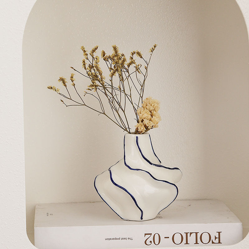 White vase with blue stripes holding dried flowers on a white surface with 'Folio-02' branding.