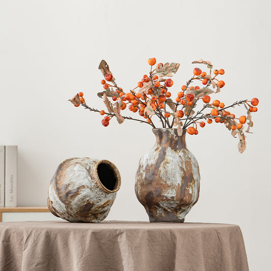 Two rustic vases with a decorative branch on a table against a plain wall.