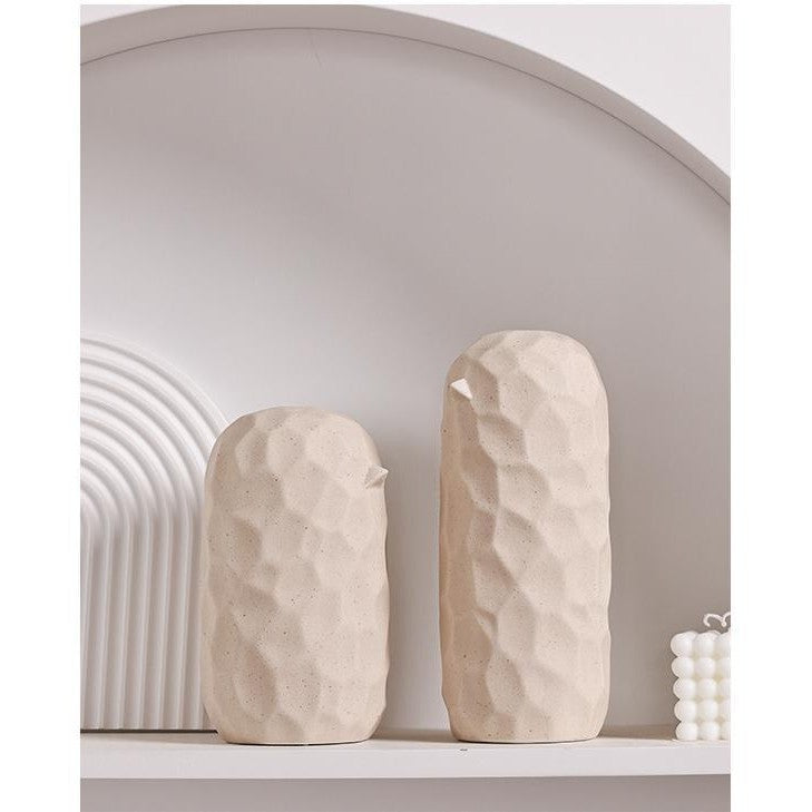 Two beige stone-like vases on a white shelf with a neutral wall background