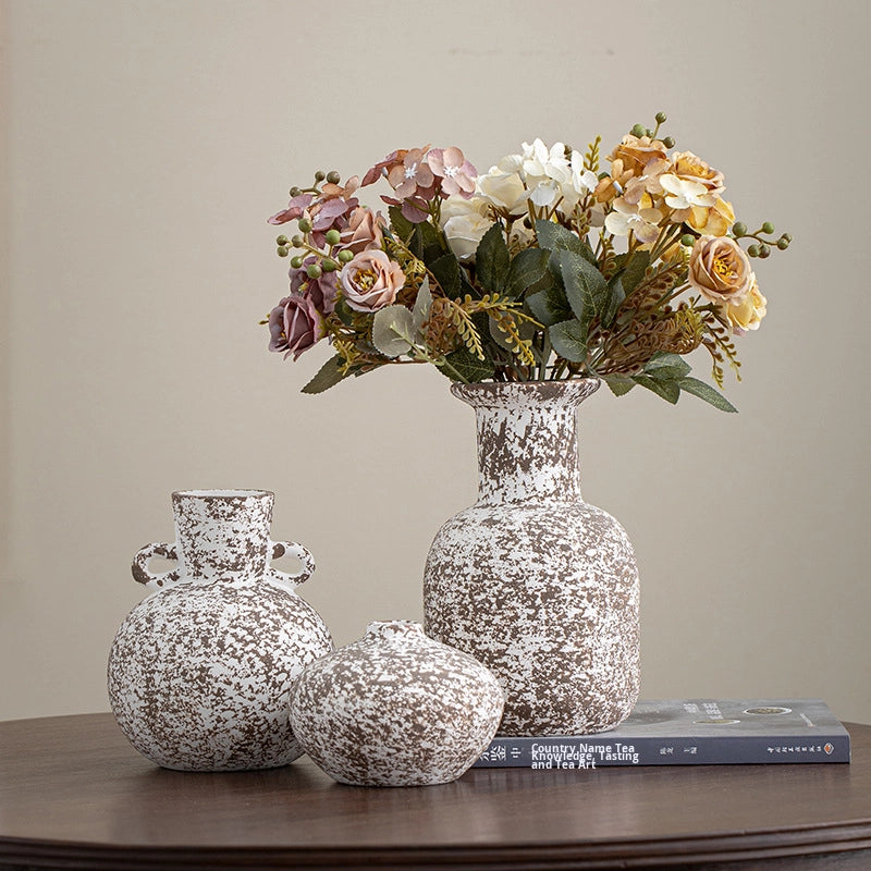Decorative speckled vases with a bouquet of flowers on a wooden surface.