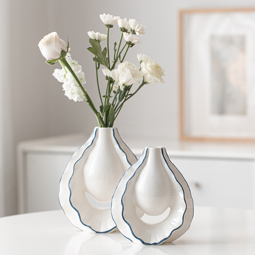 Two white vases with blue rims holding flowers on a table.