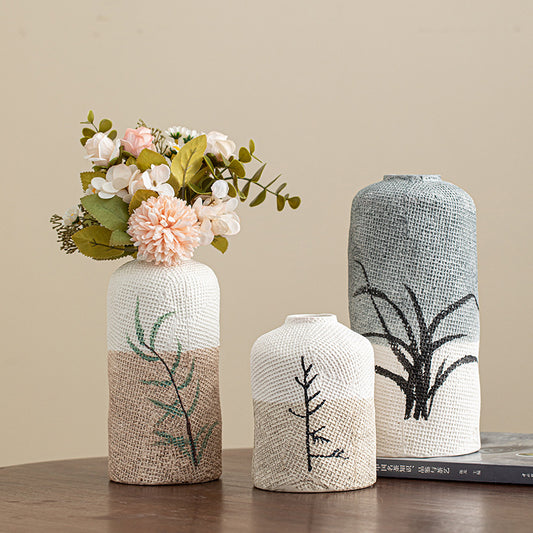 Three textured vases with floral and plant designs on a wooden surface against a beige wall.