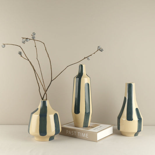 Three ceramic vases with green stripes on a beige surface and background.