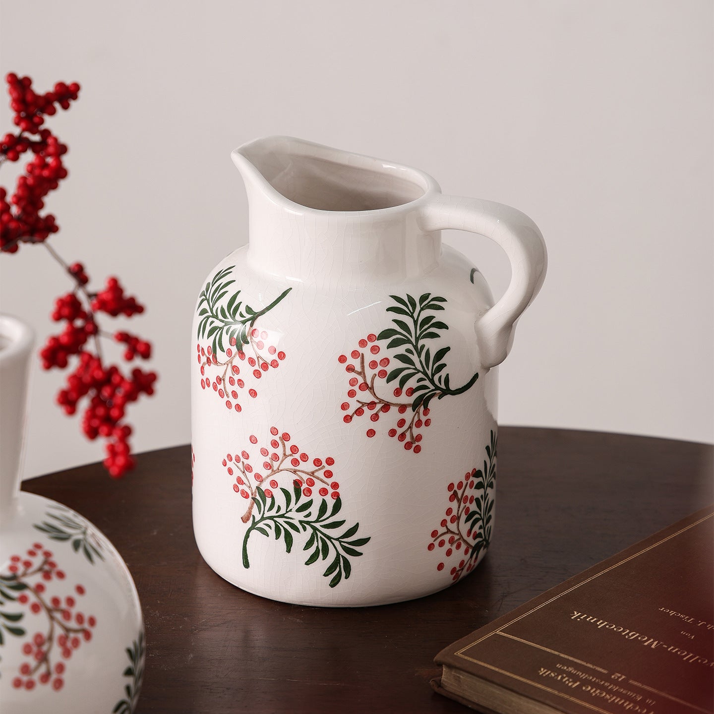 White ceramic pitcher with red and green floral patterns on a wooden surface.
