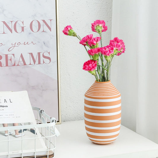 Striped vase with pink flowers on a white surface, with motivational poster in the background.