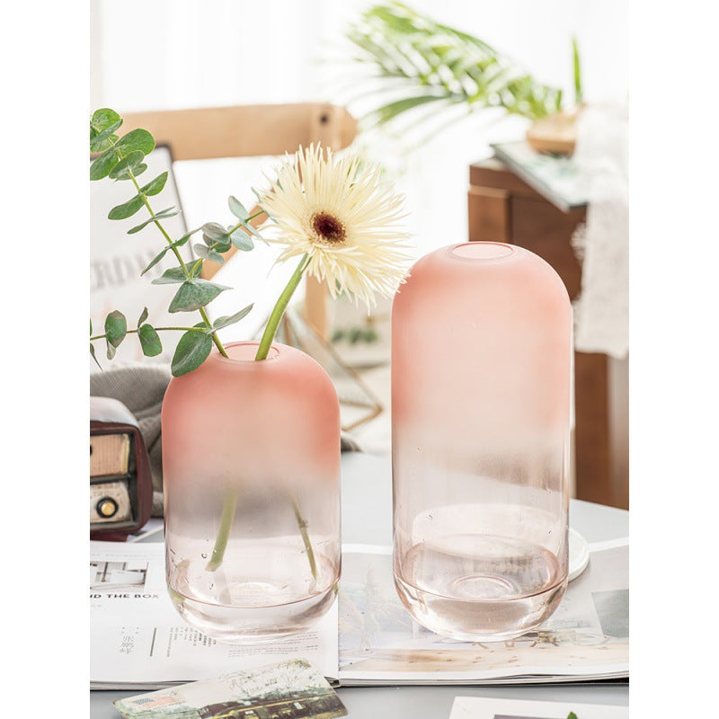 Two gradient pink vases with a plant on a table with a magazine and decorative items.