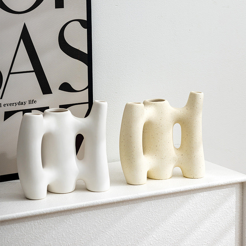 Three modern ceramic vases on a white surface with a black and white abstract art piece in the background.