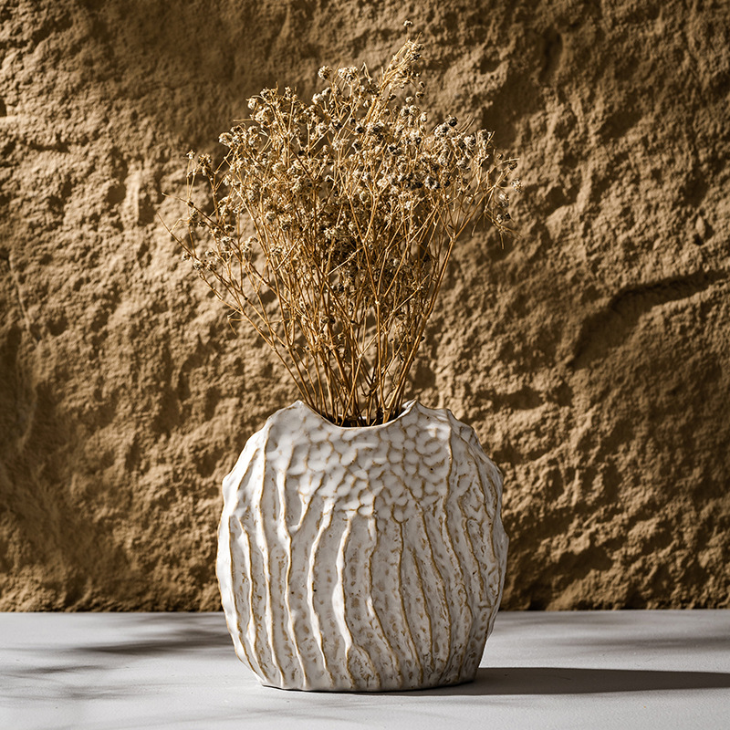 Textured ceramic vase with dried flowers against a stone wall