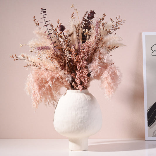 White vase with dried flowers on a light pink background
