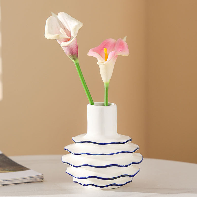 White vase with wavy design holding pink and white flowers on a beige background