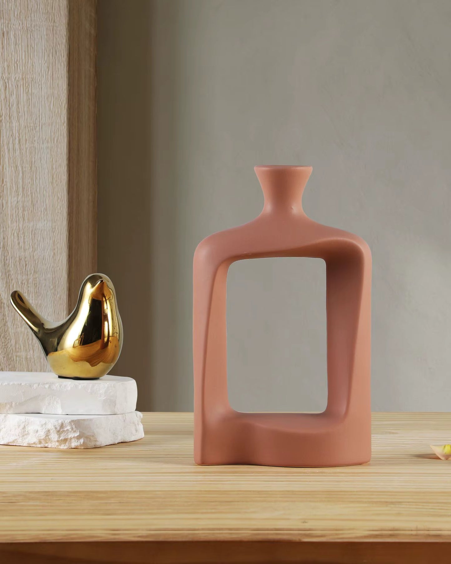 Ceramic vase with a gold bird figurine and white stones on a wooden surface.