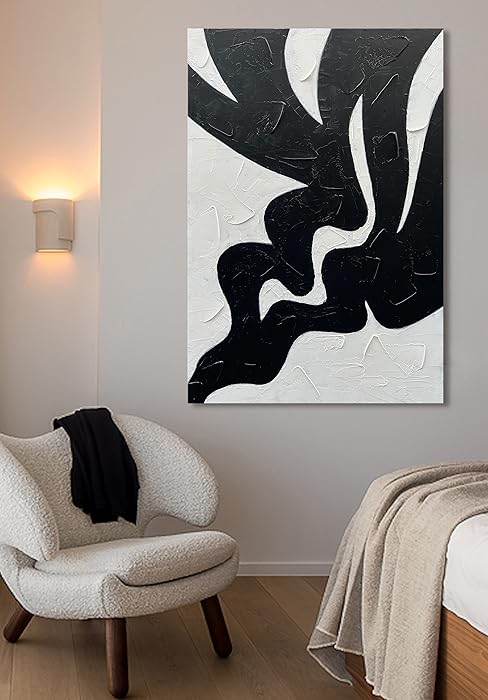 Abstract black and white painting on a wall above a chair and bed.
