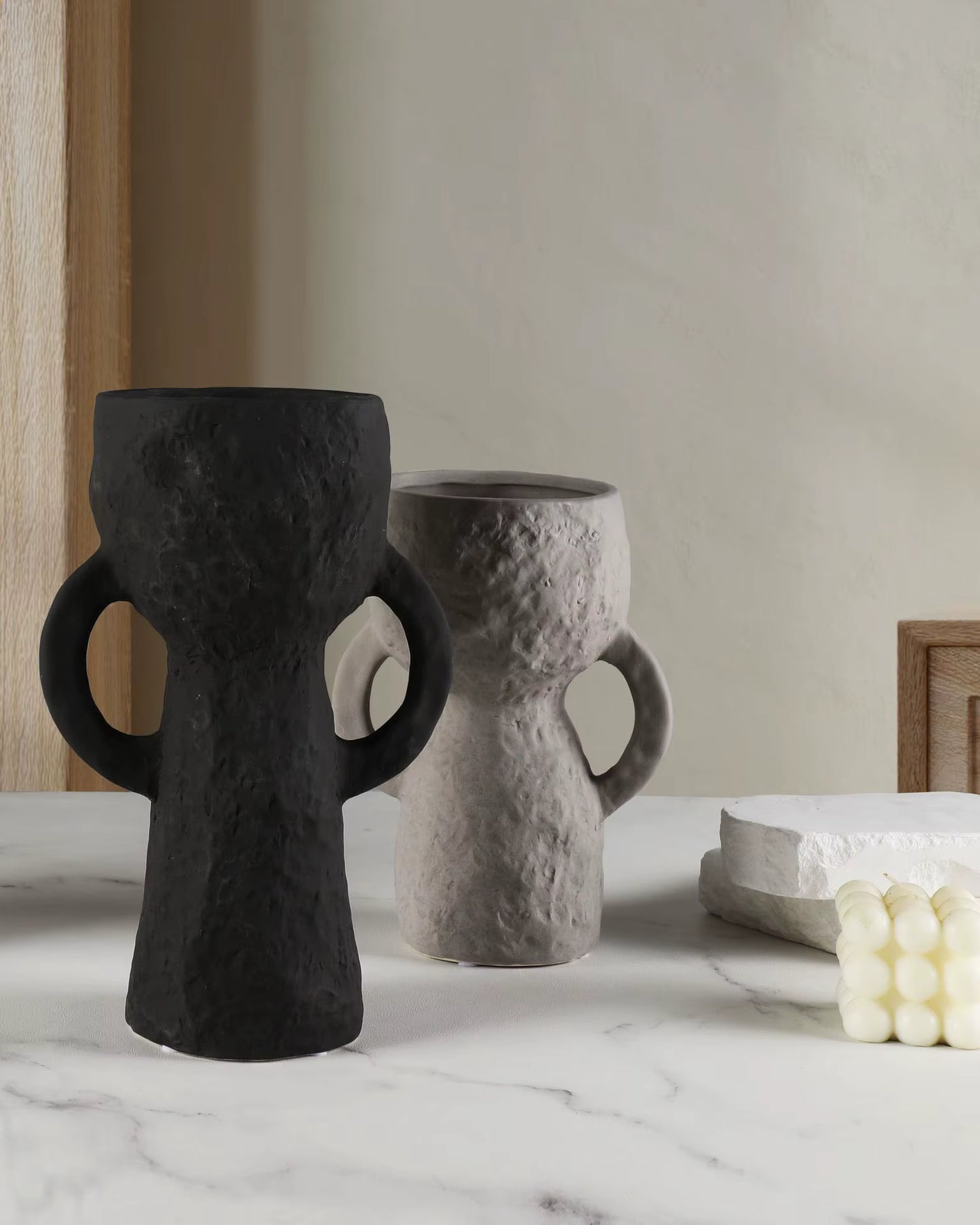 Two black and gray textured vases on a marble surface with a neutral background