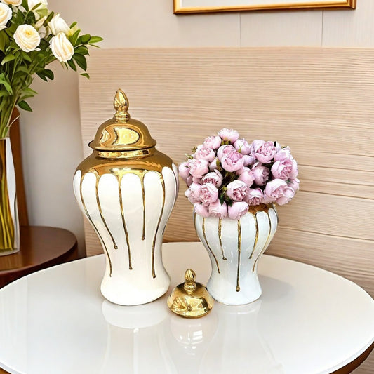 Decorative white vase with gold accents and a small white table with a gold bell and pink flowers.