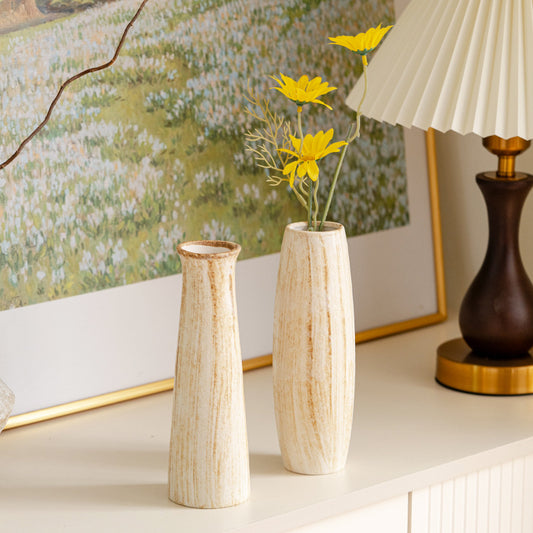 Two wooden vases with yellow flowers on a shelf, with a lamp and painting in the background.