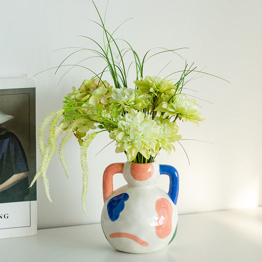 Colorful ceramic vase with floral arrangement on a white surface