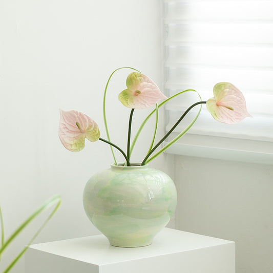 Green vase with pink flowers on a white surface