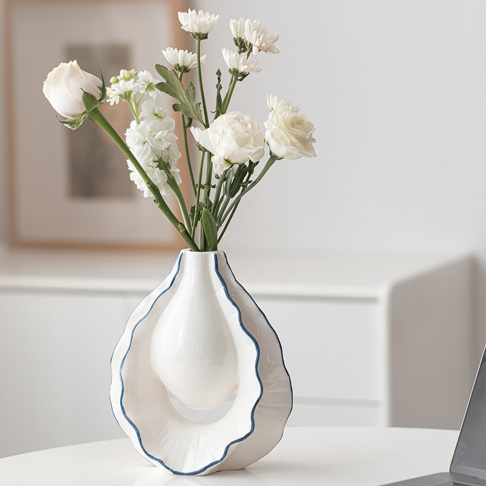 White vase with wavy design holding white flowers on a light surface.