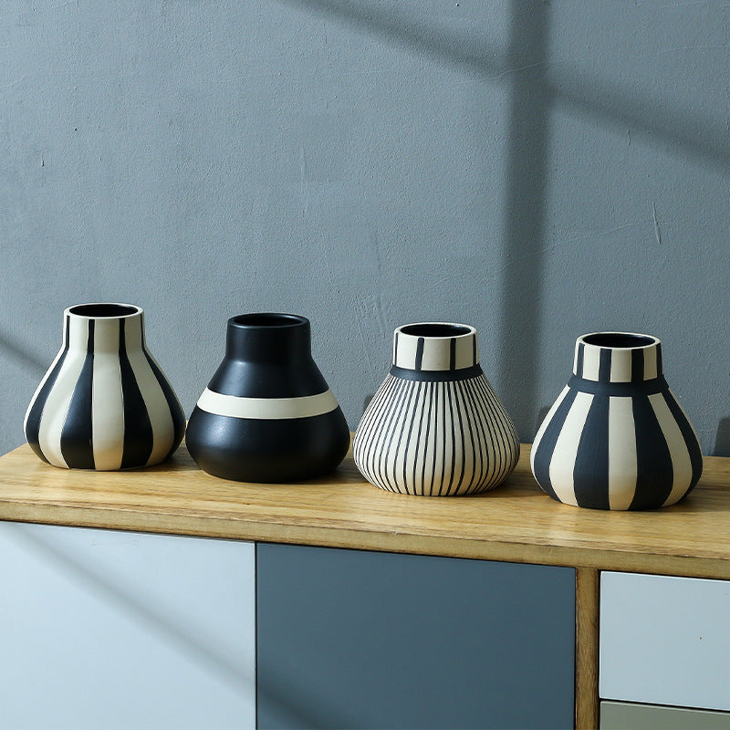 Four black and white patterned vases on a wooden surface with a gray wall background