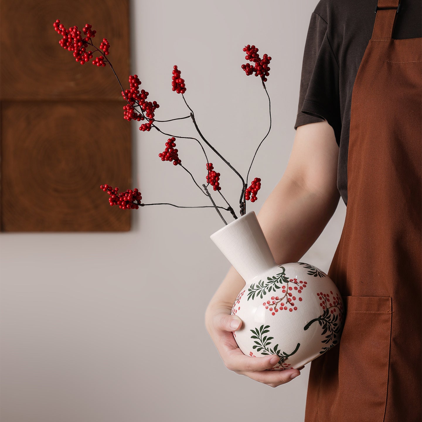 Person holding a white vase with red floral design against a neutral background