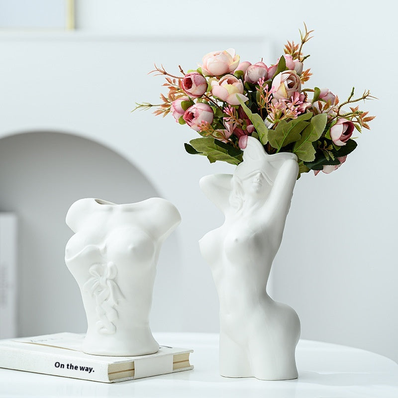 White vase shaped like a torso holding flowers on a white surface with a light gray background