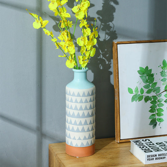 Decorative vase with geometric pattern and yellow flowers on a wooden surface.