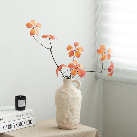 White textured vase with orange leaves on a table against a white wall