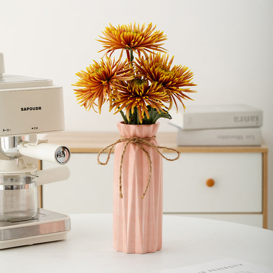 Pink vase with yellow flowers on a white surface next to a coffee machine.