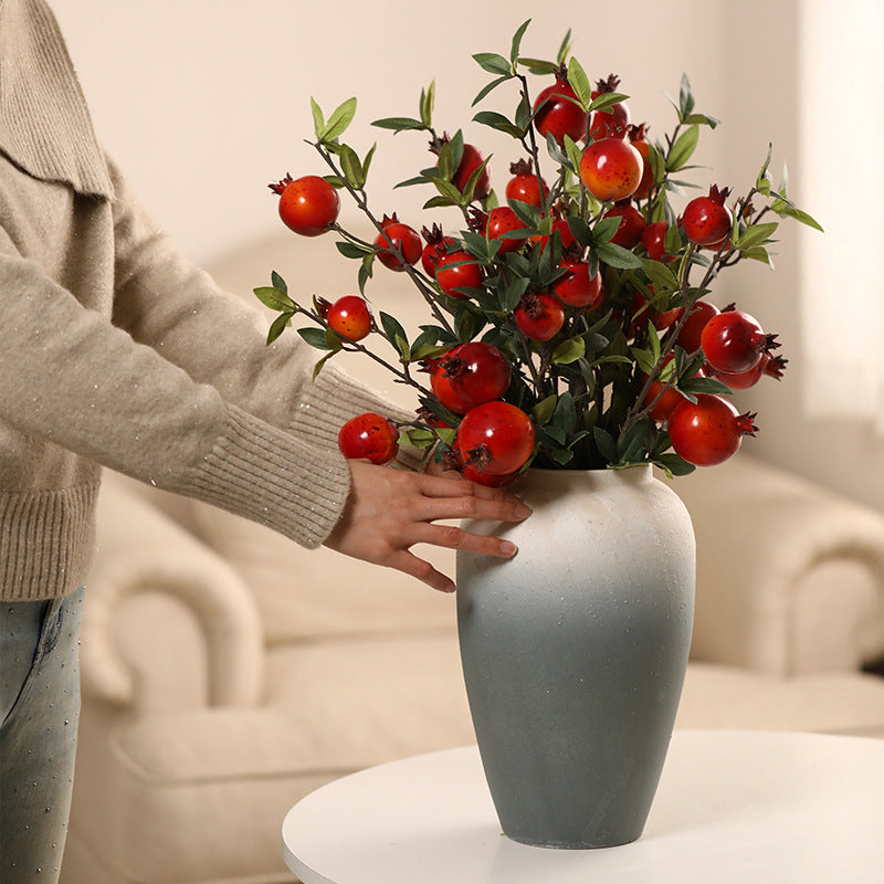 Person holding a vase with red floral arrangement on a table