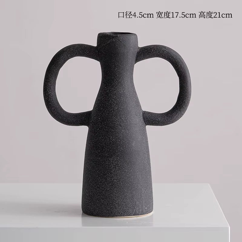 Black ceramic vase with handles on a light gray background