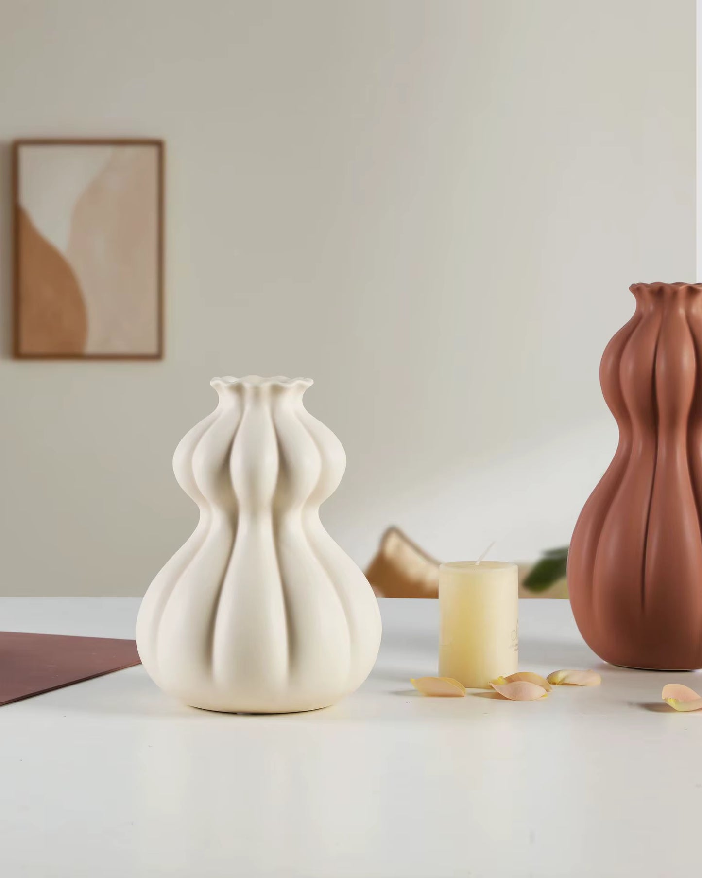 Two ceramic vases, one white and one terracotta, on a light surface with a candle and decorative elements.