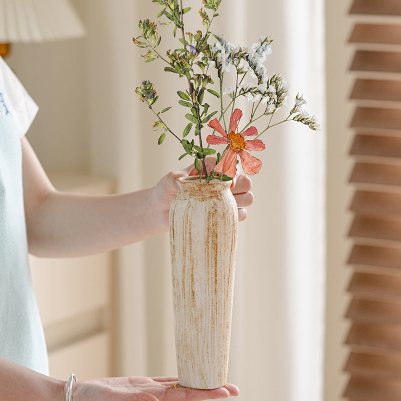 Person holding a vase with flowers against a neutral background