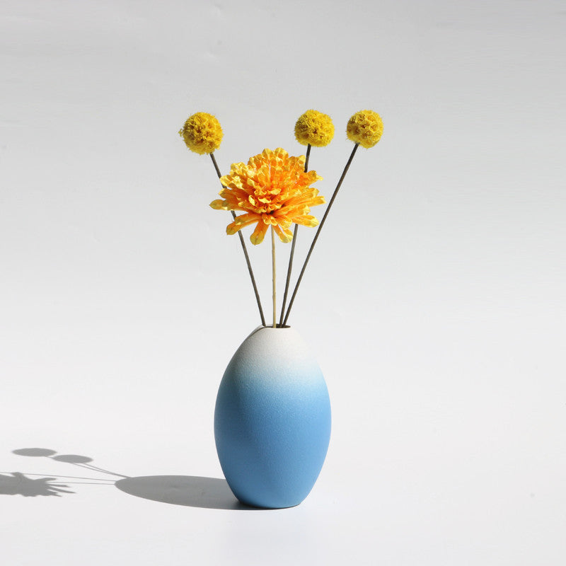 White and blue vase with yellow flowers on a light gray background