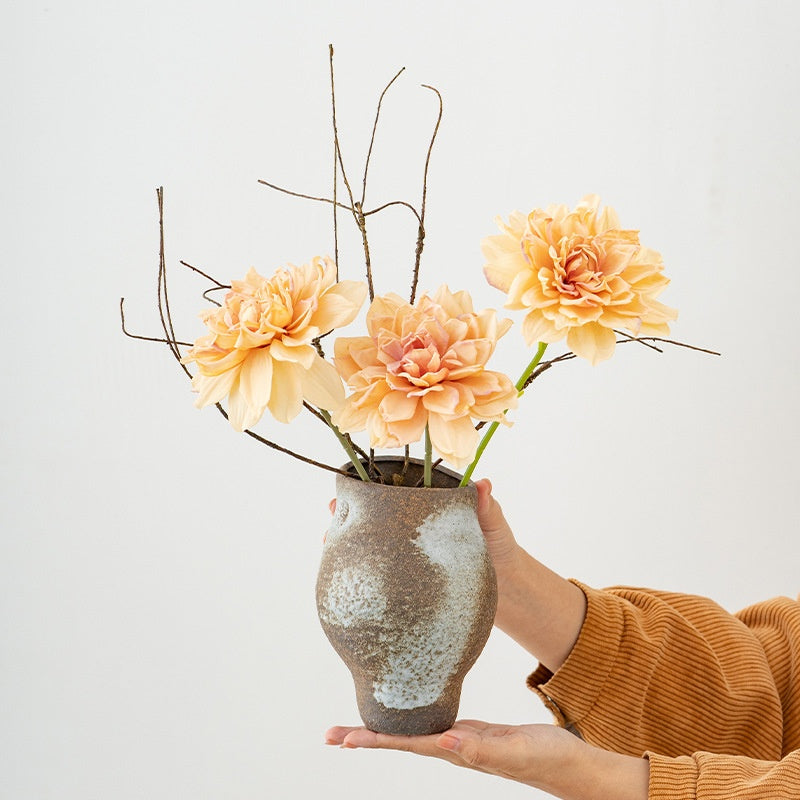 Person holding a vase with peach-colored flowers against a light background