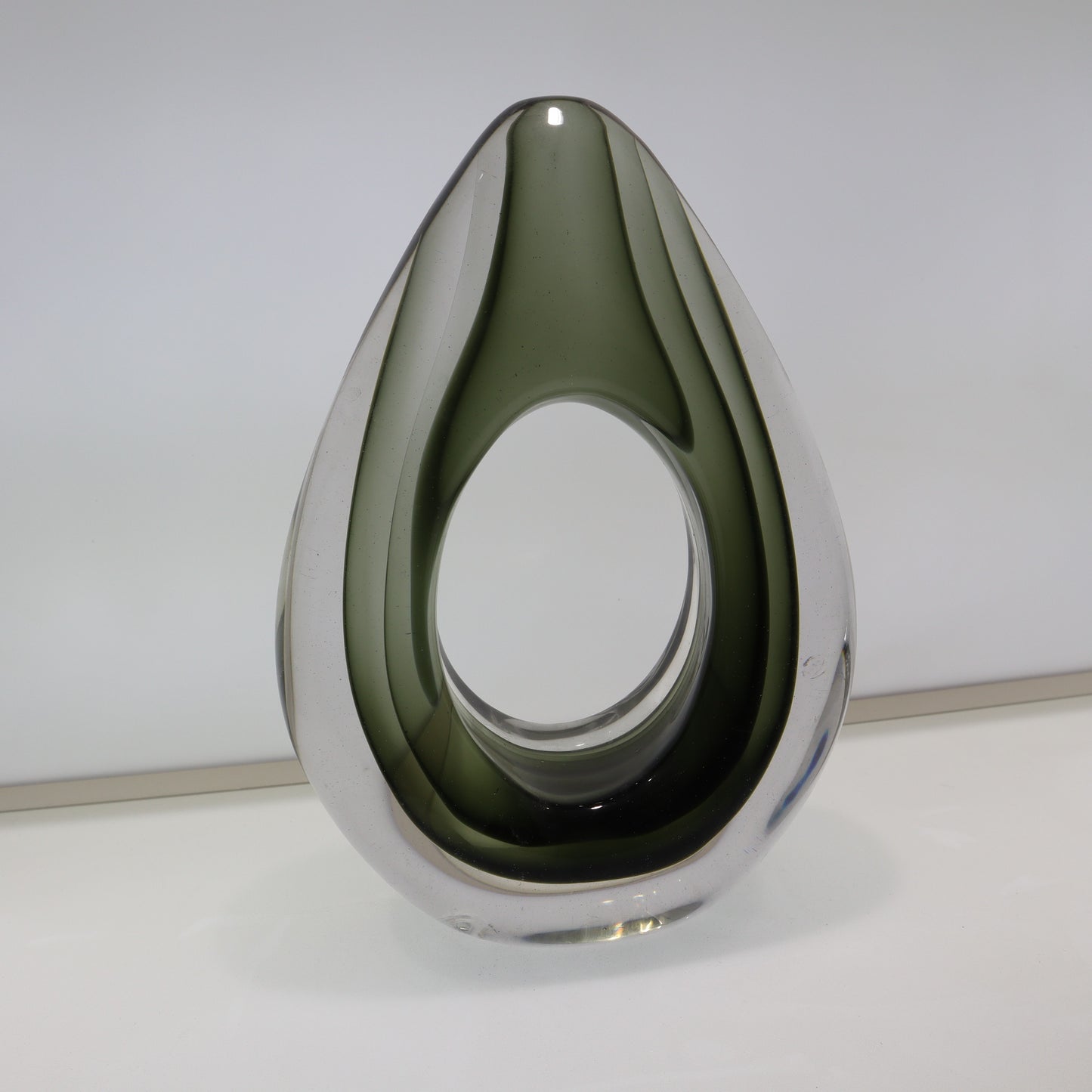 Teardrop-shaped glass object on a white surface with a light gray background