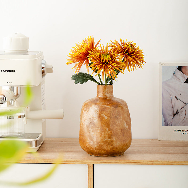 Brown vase with orange flowers on a wooden shelf next to a white appliance.
