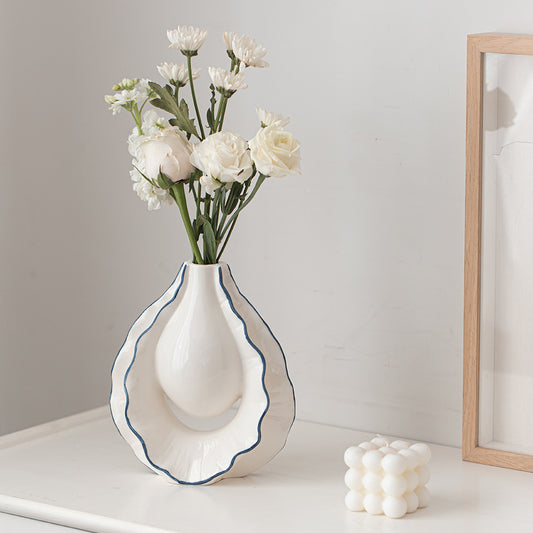 White vase with blue rim holding white flowers on a light surface with a neutral background