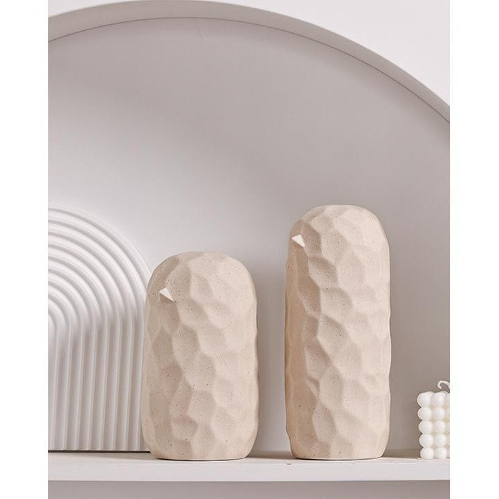 Two beige stone sculptures on a shelf with a neutral background