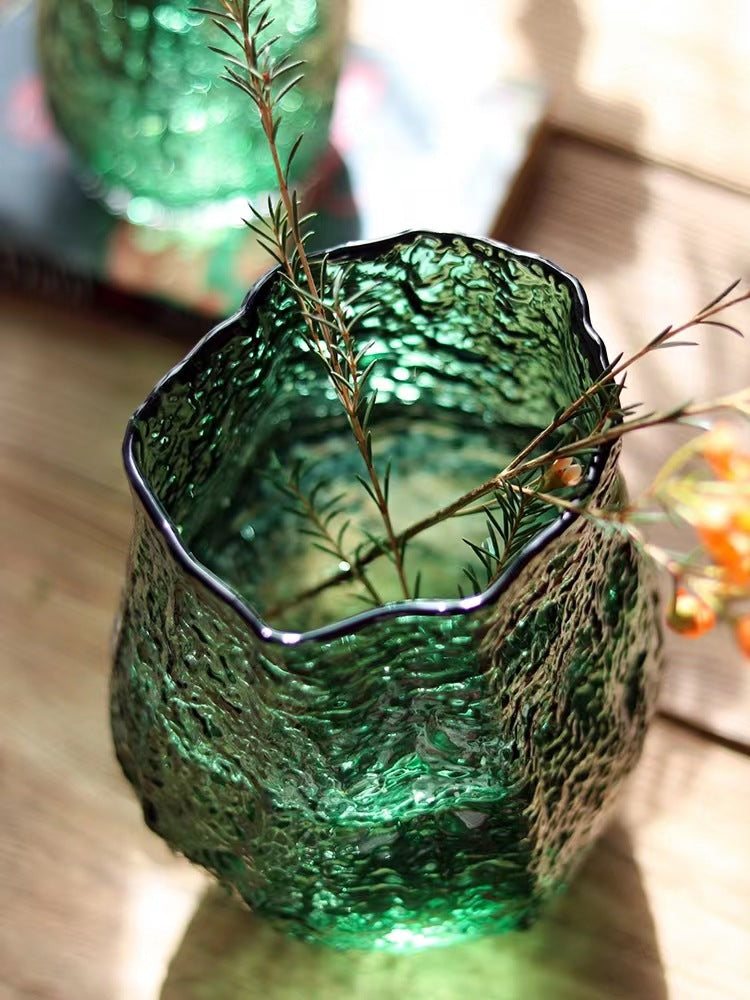 Green textured glass vase with a plant on a wooden surface