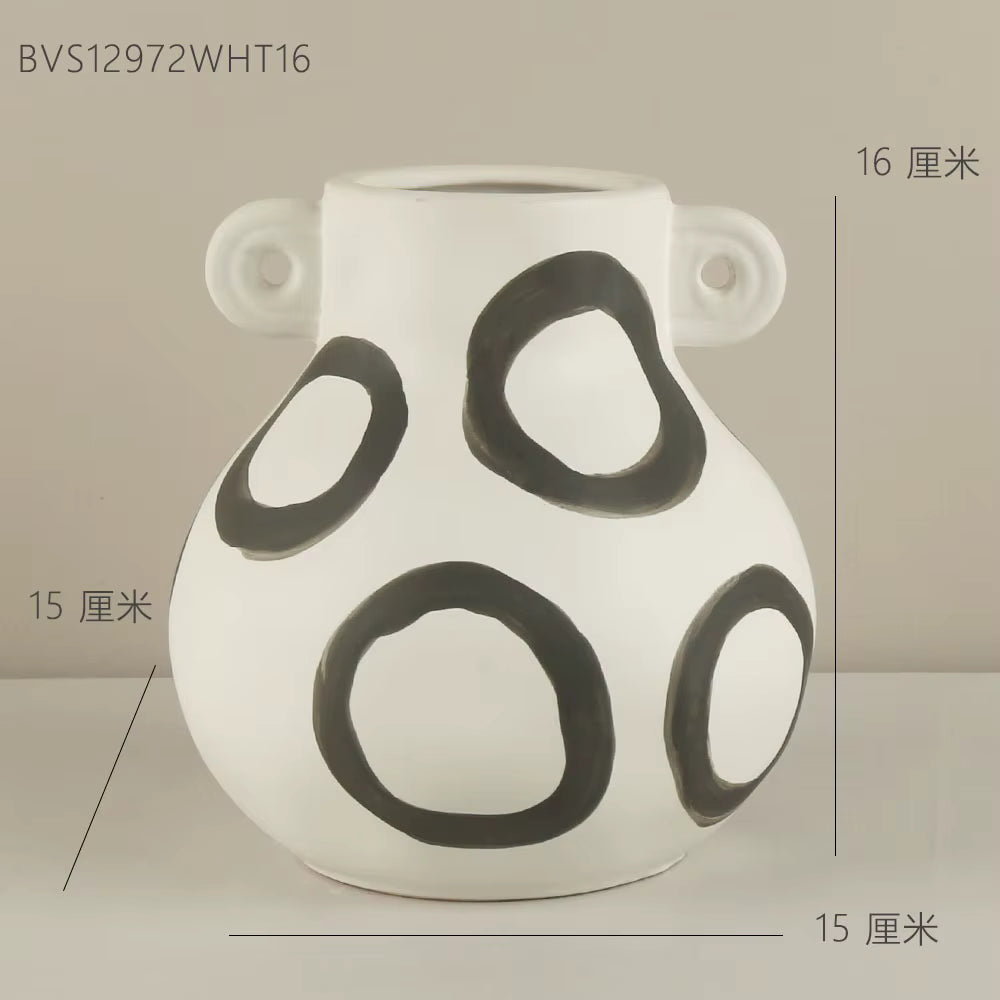 White vase with black circular patterns on a beige background